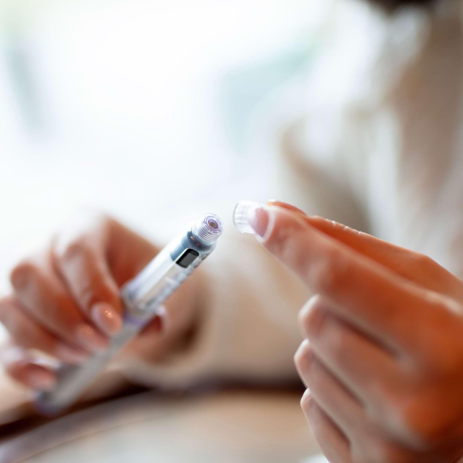 Person handling an insulin pen, attaching a needle cap, with a blurred background.
