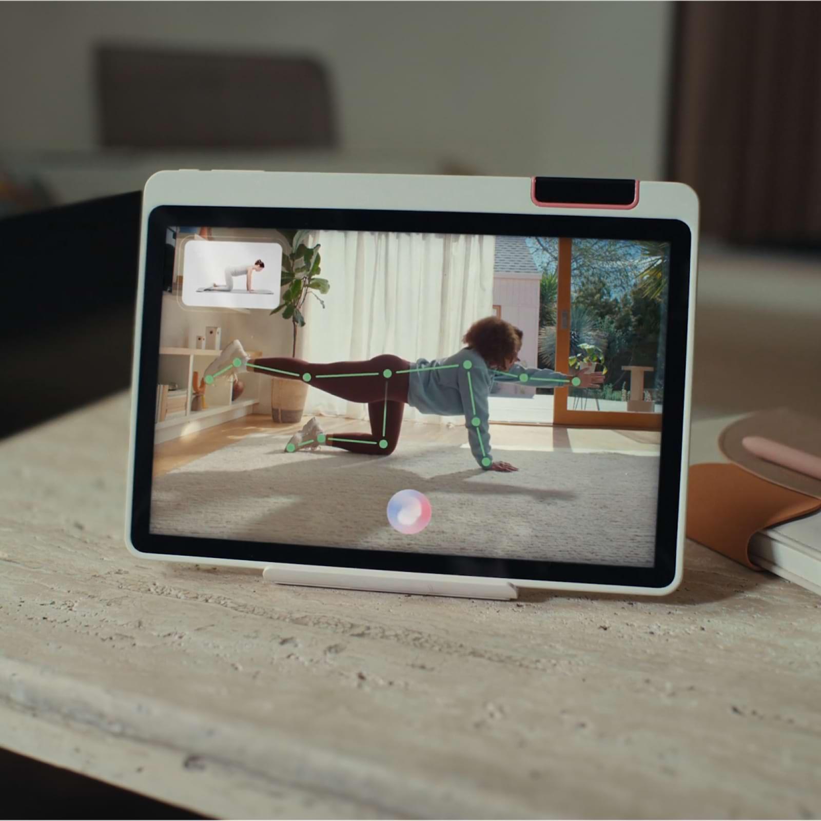 Tablet on a table showing a virtual exercise class with a person doing a plank variation, guided by digital markers on the screen.
