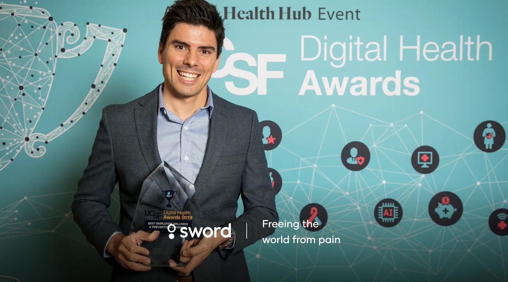 Man holding an award at the UCSF Digital Health Awards event, standing in front of a blue backdrop with logos and text.