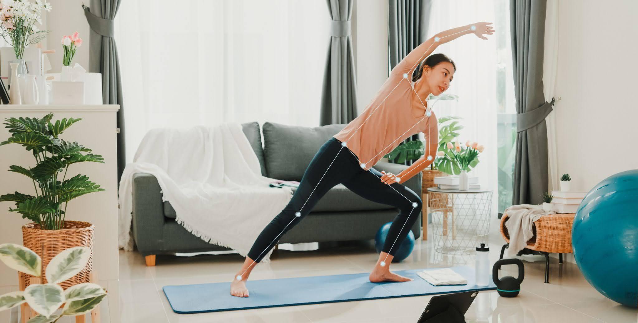 Woman practicing yoga on a mat in a living room, surrounded by plants, exercise ball, and kettlebell, with natural light from windows.